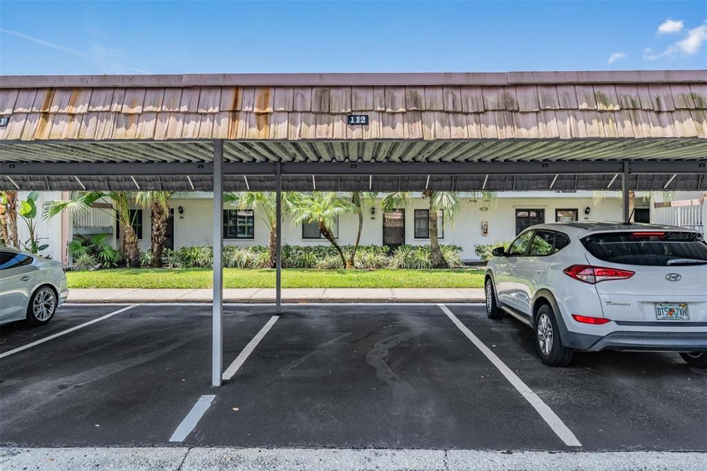 A covered parking area with two cars parked under a weathered wooden roof structure — 112 LAKEVIEW PLACE UNIT 12, OLDSMAR, FL