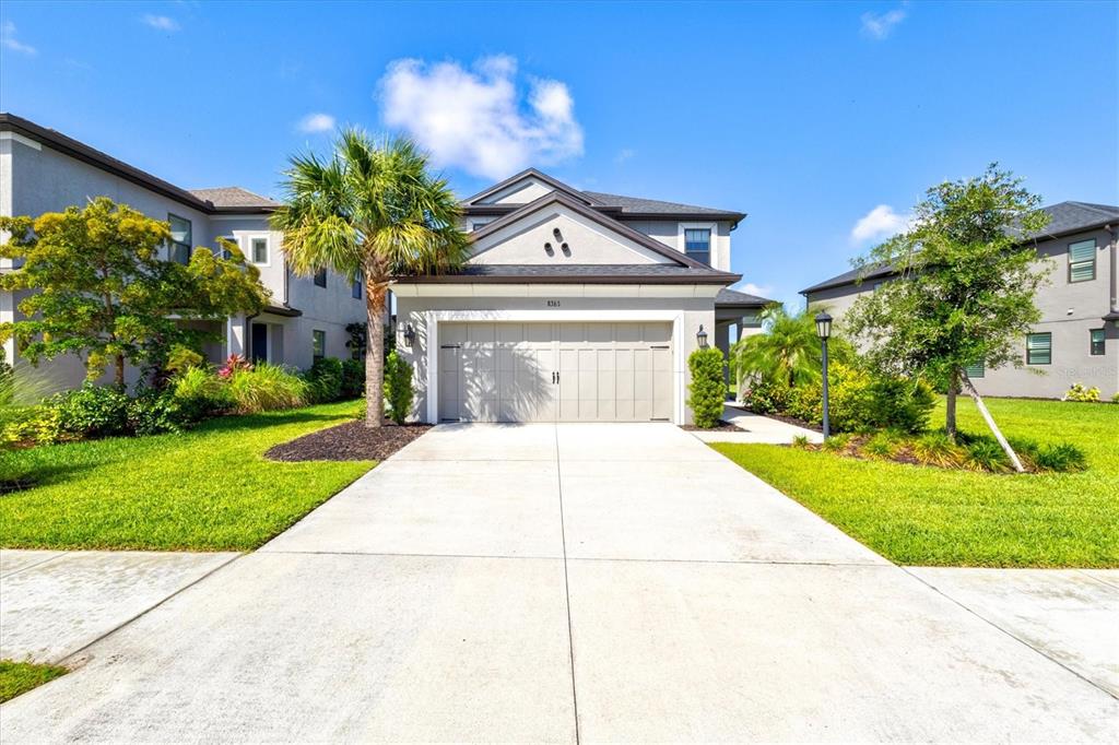 A two-story suburban house with a beige garage, palm tree, and green lawn — 8363 VELDA TRAIL, SARASOTA, FL