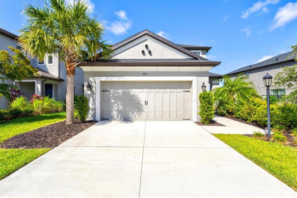 A beige house exterior features a two-car garage, a palm tree, and a concrete driveway — 8363 VELDA TRAIL, SARASOTA, FL