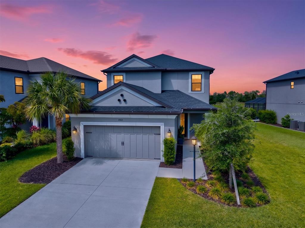 A two-story suburban house with a gray garage and a palm tree at sunset — 8363 VELDA TRAIL, SARASOTA, FL