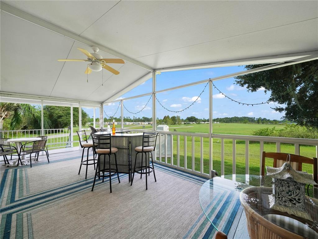 A screened-in porch features a bar set, patio furniture, and views of a grassy field — 15 PINK LADY LANE, LAKE WALES, FL