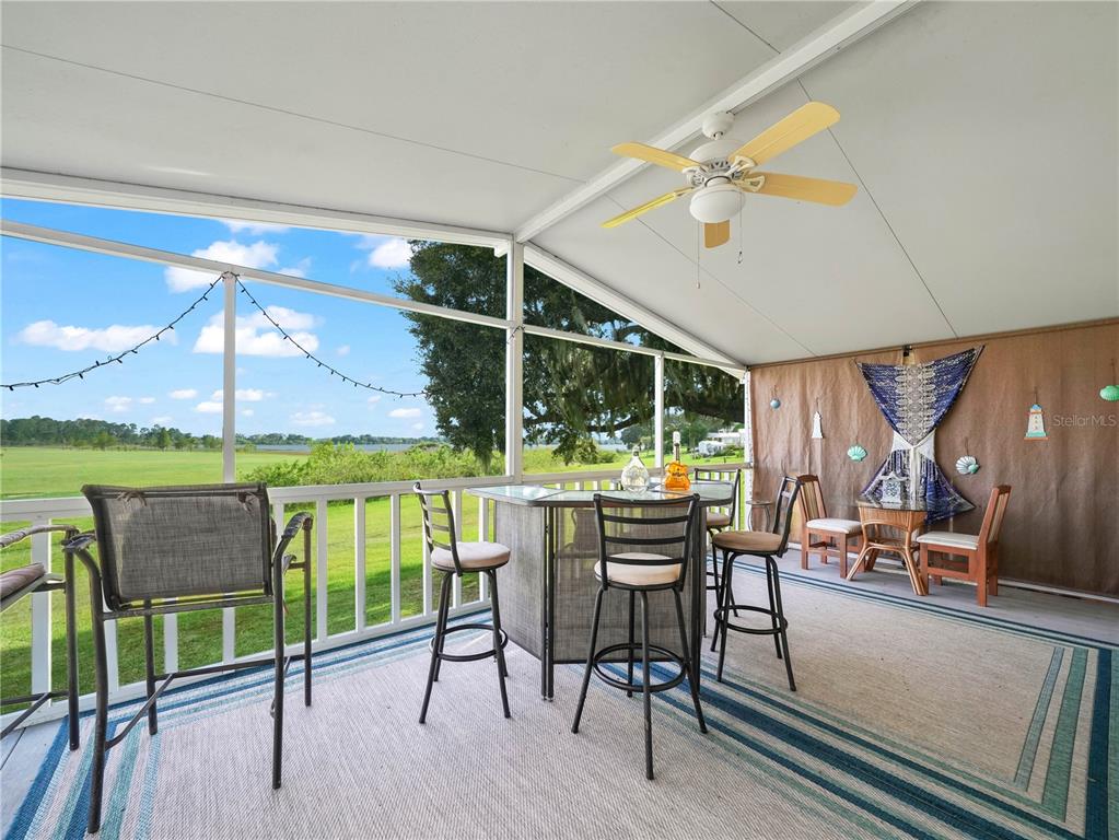 A screened-in porch features a bar set, ceiling fan, and views of a grassy field — 15 PINK LADY LANE, LAKE WALES, FL