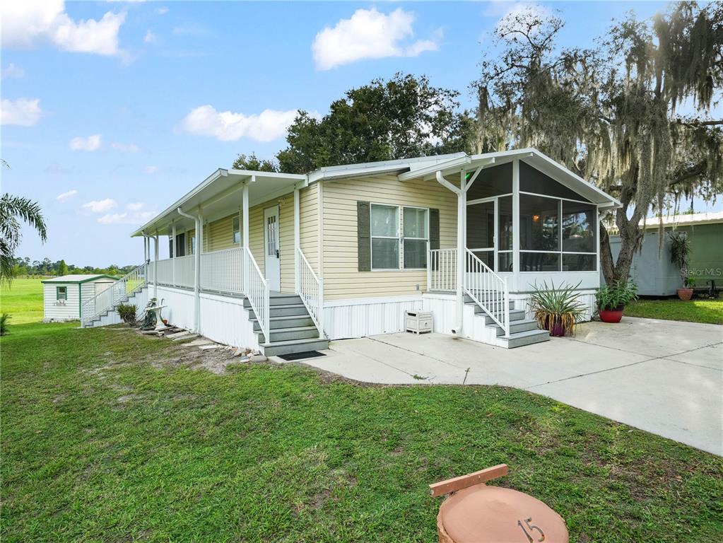 A light yellow manufactured home features a screened-in porch, a concrete driveway, and white railings — 15 PINK LADY LANE, LAKE WALES, FL