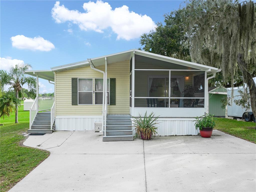 A light yellow manufactured home features a screened-in porch and a concrete driveway — 15 PINK LADY LANE, LAKE WALES, FL