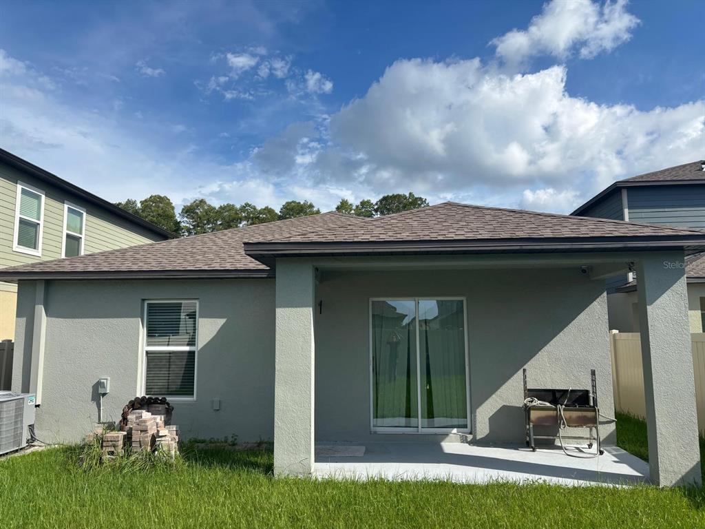 The exterior rear view of a gray stucco house features a covered patio and lawn — 22481 STORYBOOK CABIN WAY, LAND O LAKES, FL