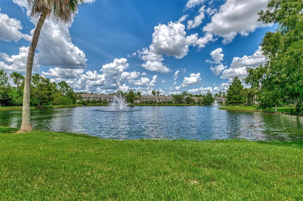 A pond with two fountains is surrounded by green grass, trees, and apartment buildings — 8911 MANOR LOOP UNIT 207, LAKEWOOD RANCH, FL