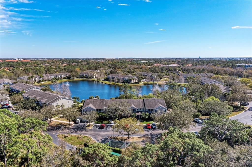 An aerial view shows multi-story residential buildings surrounding a central lake with fountains — 8911 MANOR LOOP UNIT 207, LAKEWOOD RANCH, FL