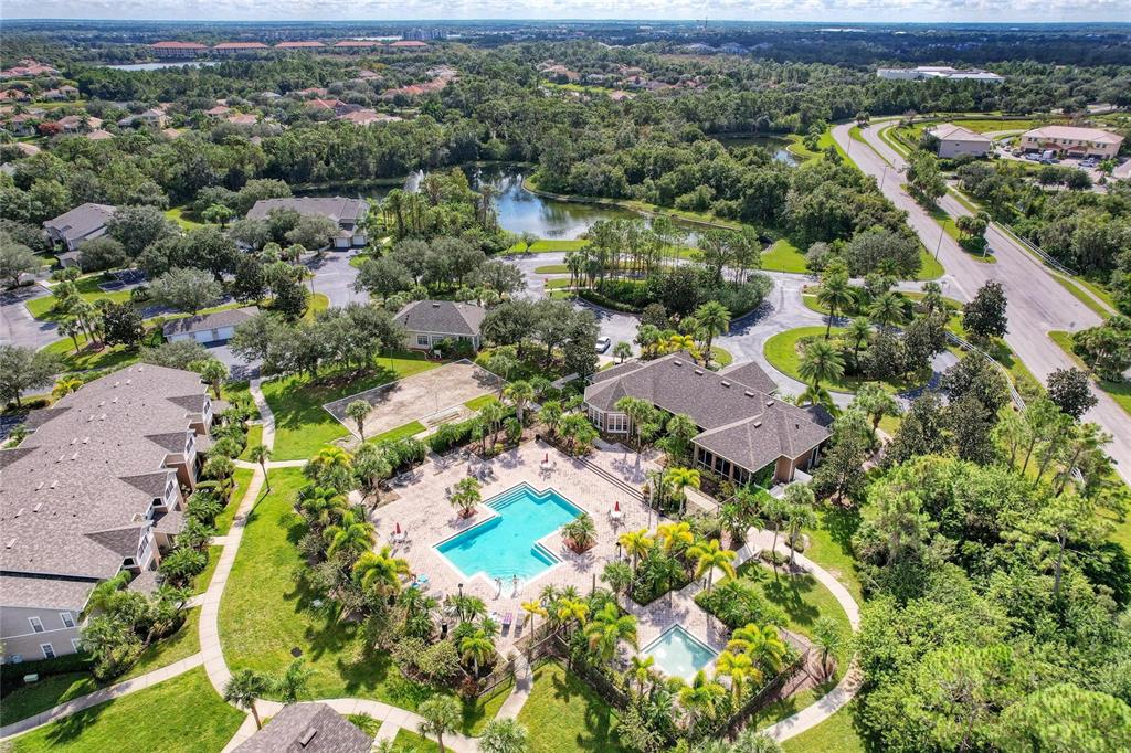 An aerial view shows a community pool, clubhouse, and surrounding residential buildings with lush landscaping — 8911 MANOR LOOP UNIT 207, LAKEWOOD RANCH, FL
