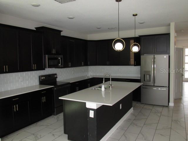 A kitchen features dark cabinetry, white countertops, a central island, and stainless steel appliances — 8982 CABOT CLIFFS DRIVE, DAVENPORT, FL
