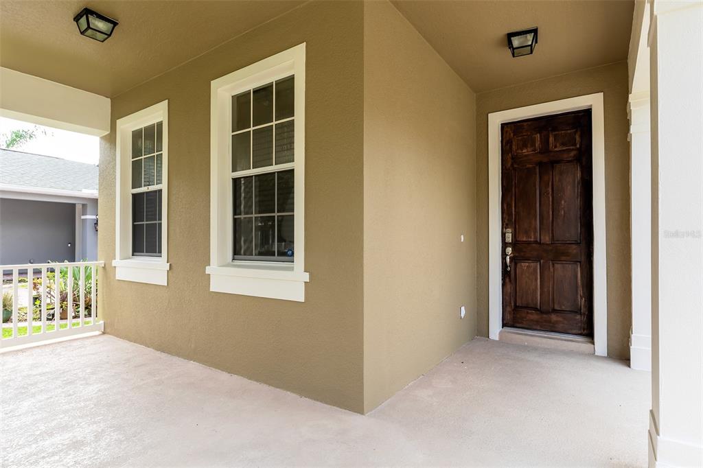A covered front porch features a dark wood door, two windows, and beige exterior walls — 13844 AMELIA POND DRIVE, WINDERMERE, FL