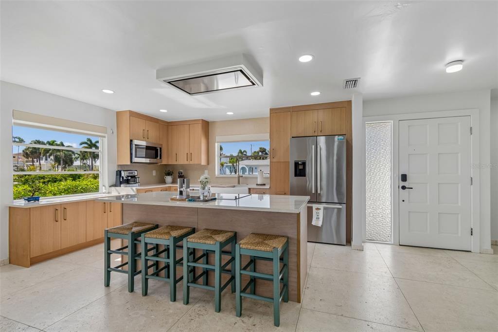 A kitchen features light wood cabinets, a central island with four stools, and stainless appliances — 114 8TH STREET, BELLEAIR BEACH, FL