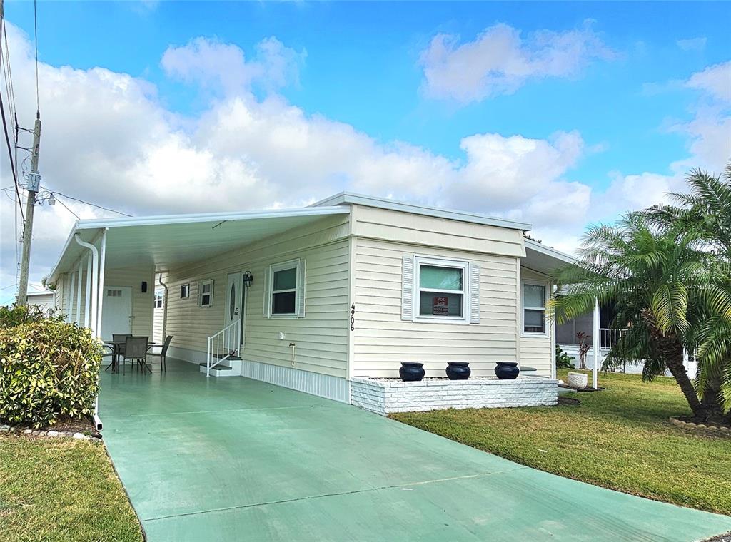A light-colored mobile home with a green carport and a small front lawn — 4906 E 7TH A STREET E UNIT 712, BRADENTON, FL