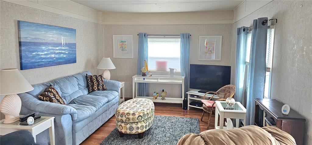 A living room features a blue sofa, patterned ottoman, television, and light-colored walls — 4906 E 7TH A STREET E UNIT 712, BRADENTON, FL
