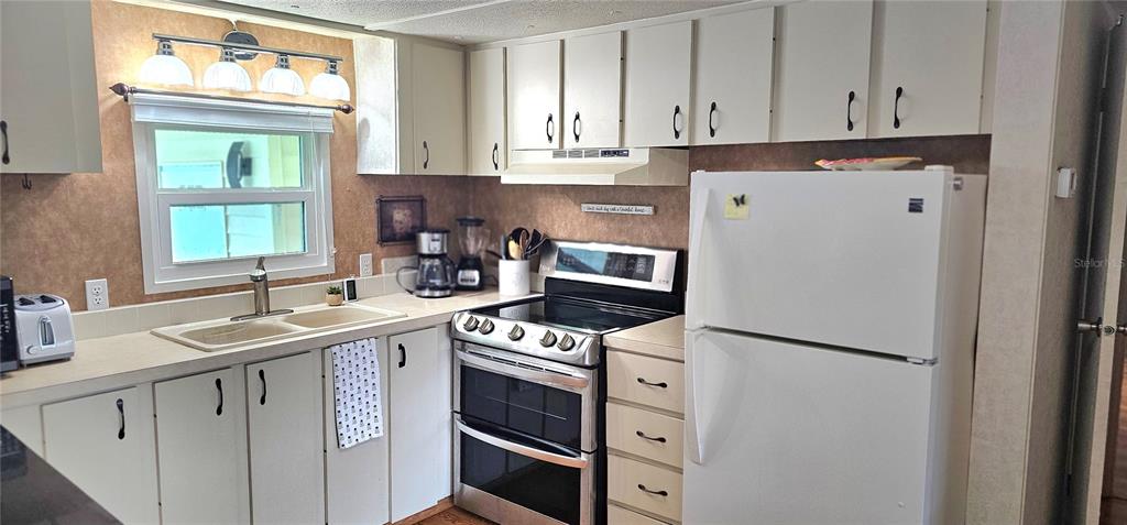 A kitchen features white cabinets, a double sink, a white stove, and a white refrigerator — 4906 E 7TH A STREET E UNIT 712, BRADENTON, FL