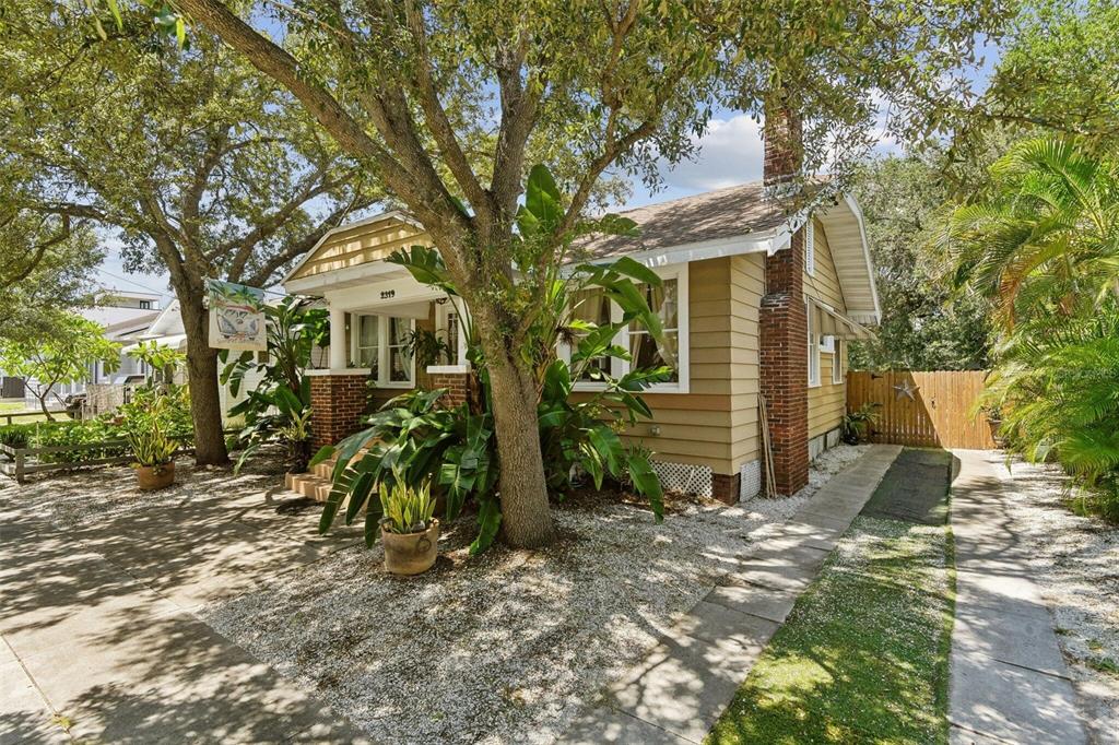 A tan bungalow with a brick chimney and front porch sits behind a large tree — 2319 W NORTH B STREET, TAMPA, FL
