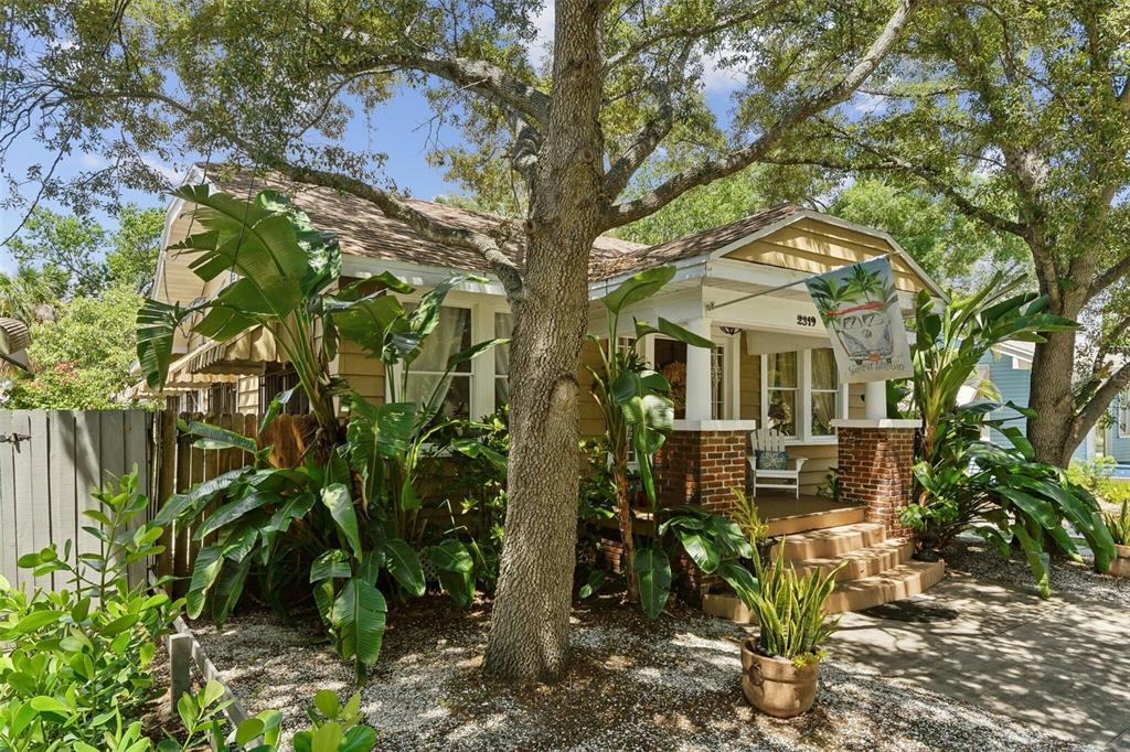 A tan bungalow with a brick-columned front porch, large trees, and lush tropical landscaping — 2319 W NORTH B STREET, TAMPA, FL
