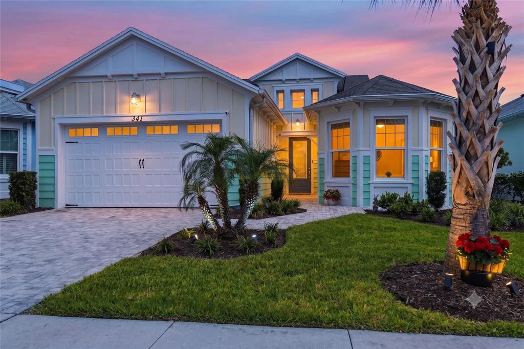 A single-story house with a two-car garage, light siding, and a paved walkway at dusk — 341 COMPASS ROSE DRIVE, DAYTONA BEACH, FL