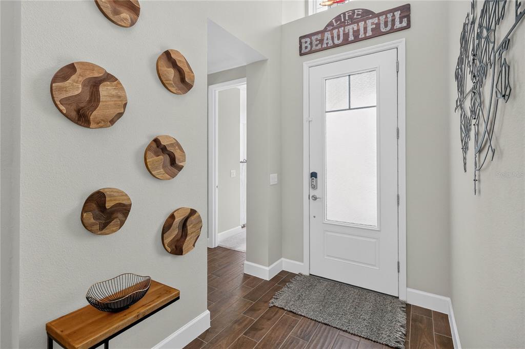 An entryway features wood-toned wall art, a floating shelf, and a white front door — 341 COMPASS ROSE DRIVE, DAYTONA BEACH, FL