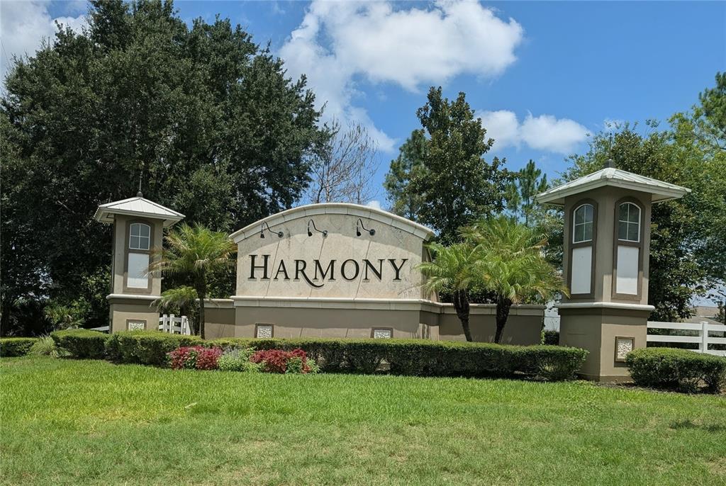 A stone monument sign for the Harmony community stands between two decorative towers and landscaping — 3214 NEEDLEGRASS LANE, HARMONY, FL