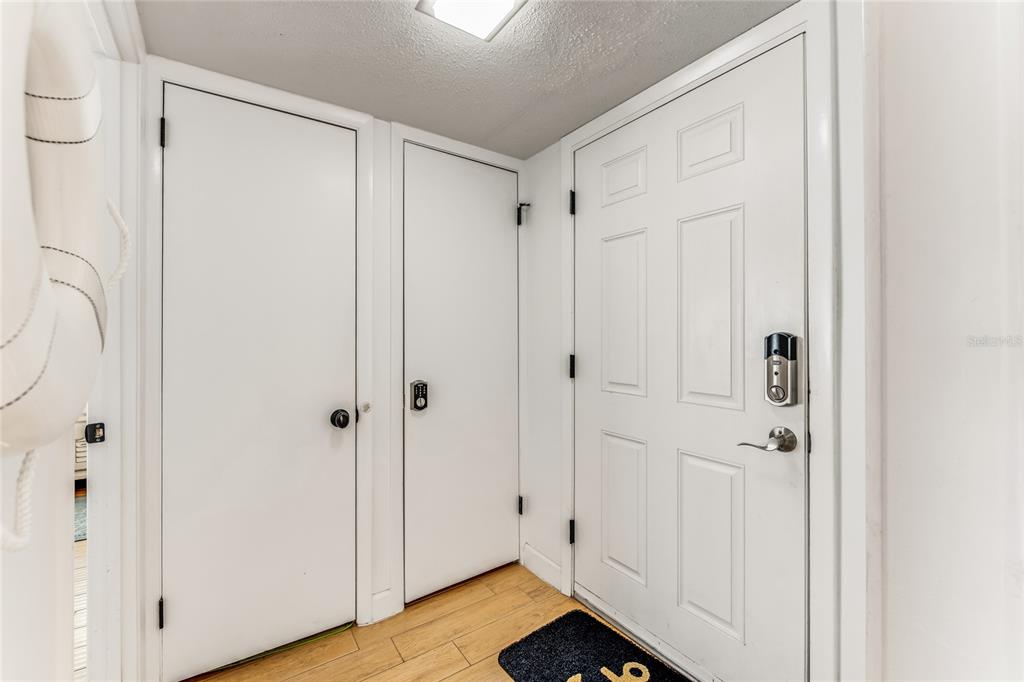 A hallway features three white doors, light wood flooring, and a smart lock — 935 OCEAN SHORE BOULEVARD UNIT 303, ORMOND BEACH, FL