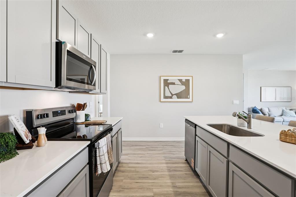 A kitchen features gray cabinets, white countertops, stainless steel appliances, and light wood-look flooring — 140 FLAG LILLY LANE, UMATILLA, FL