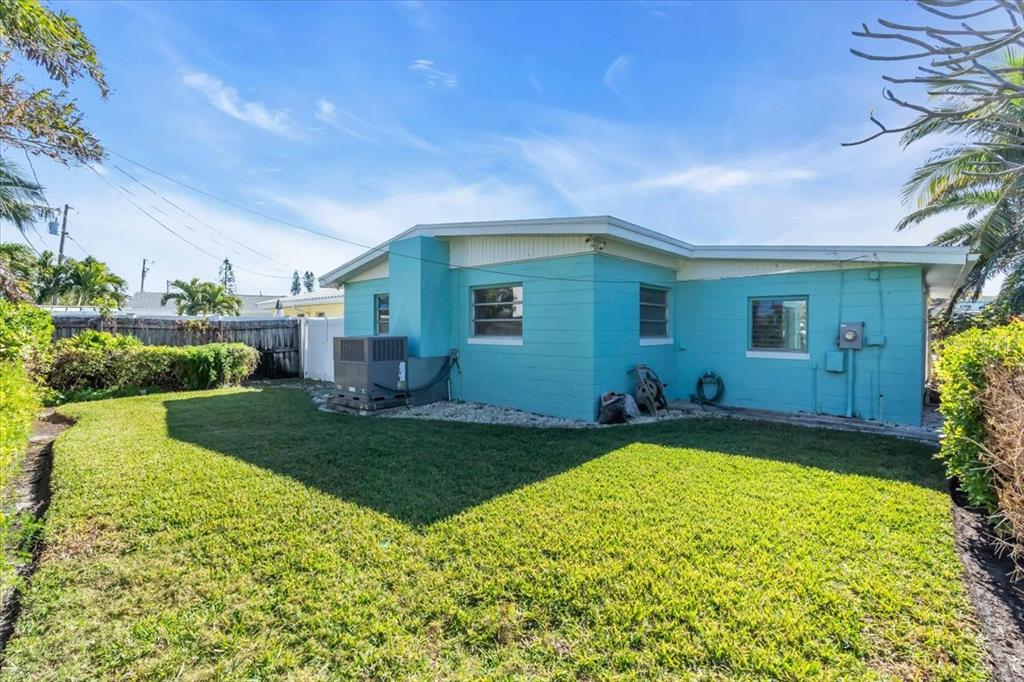 The exterior of a turquoise-painted house features a grassy backyard and an air conditioning unit — 11435 2ND STREET E, TREASURE ISLAND, FL