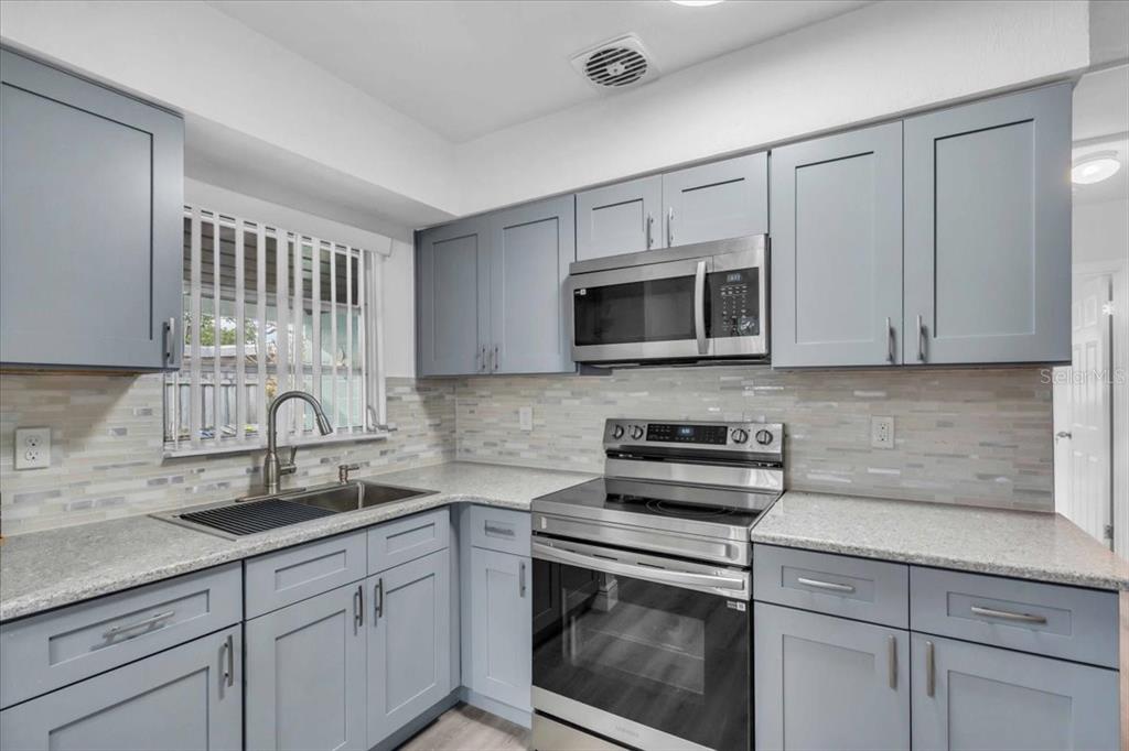 A kitchen with light blue cabinets, stainless steel appliances, and a tiled backsplash — 11435 2ND STREET E, TREASURE ISLAND, FL