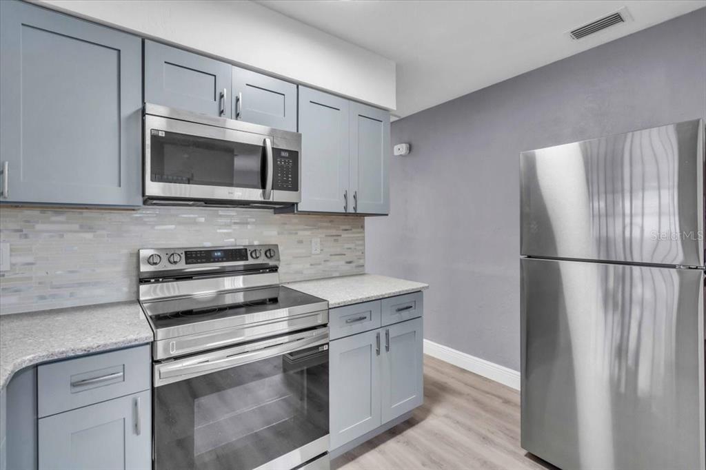 A kitchen features light blue cabinets, stainless steel appliances, and a light-colored tile backsplash — 11435 2ND STREET E, TREASURE ISLAND, FL