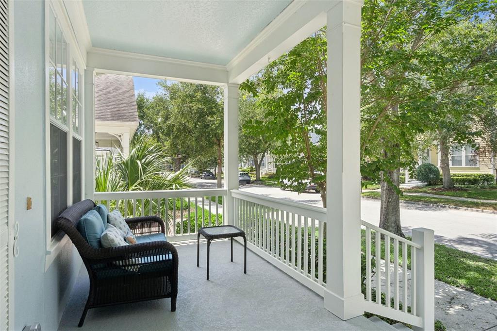 A covered front porch features a wicker chair, a small table, and white railings — 930 CROTON ROAD, CELEBRATION, FL