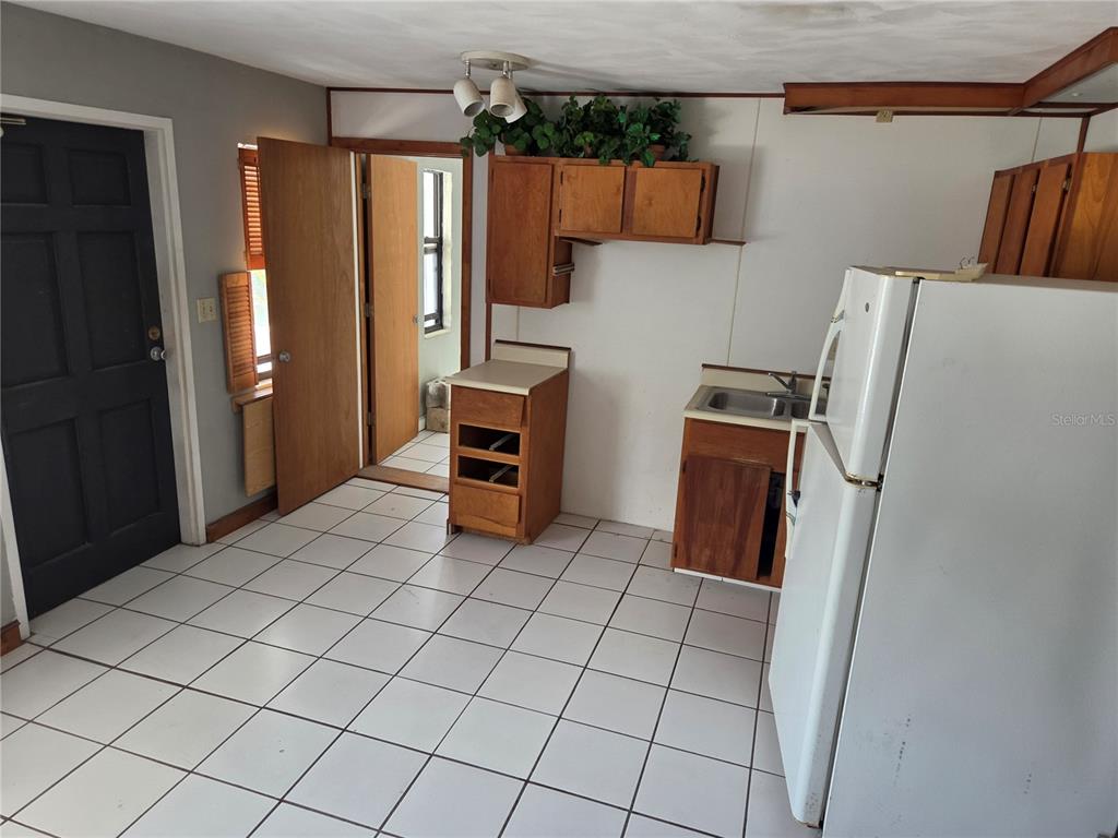 A kitchen with white tile floors, wooden cabinets, a white refrigerator, and a dark door — 580 BAY ESPLANADE, CLEARWATER BEACH, FL