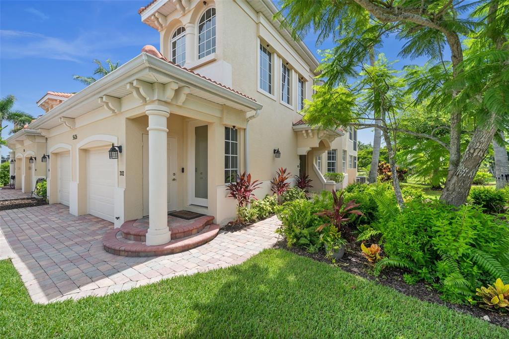 A two-story stucco townhouse with a paved driveway, garage, and lush tropical landscaping — 5626 CAPE HARBOUR DRIVE UNIT 102, CAPE CORAL, FL