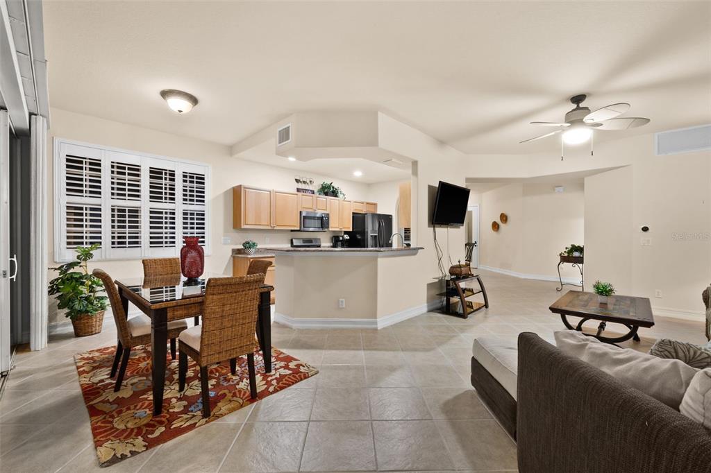 An open-concept living and dining area features tile flooring, a kitchen island, and wicker chairs — 5626 CAPE HARBOUR DRIVE UNIT 102, CAPE CORAL, FL