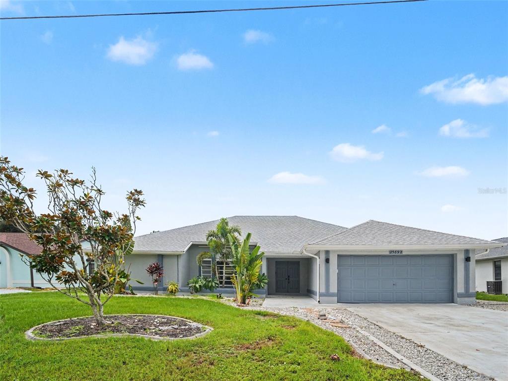A single-story house with a gray garage, a front lawn, and landscaping under a blue sky — 25892 AYSEN DRIVE, PUNTA GORDA, FL