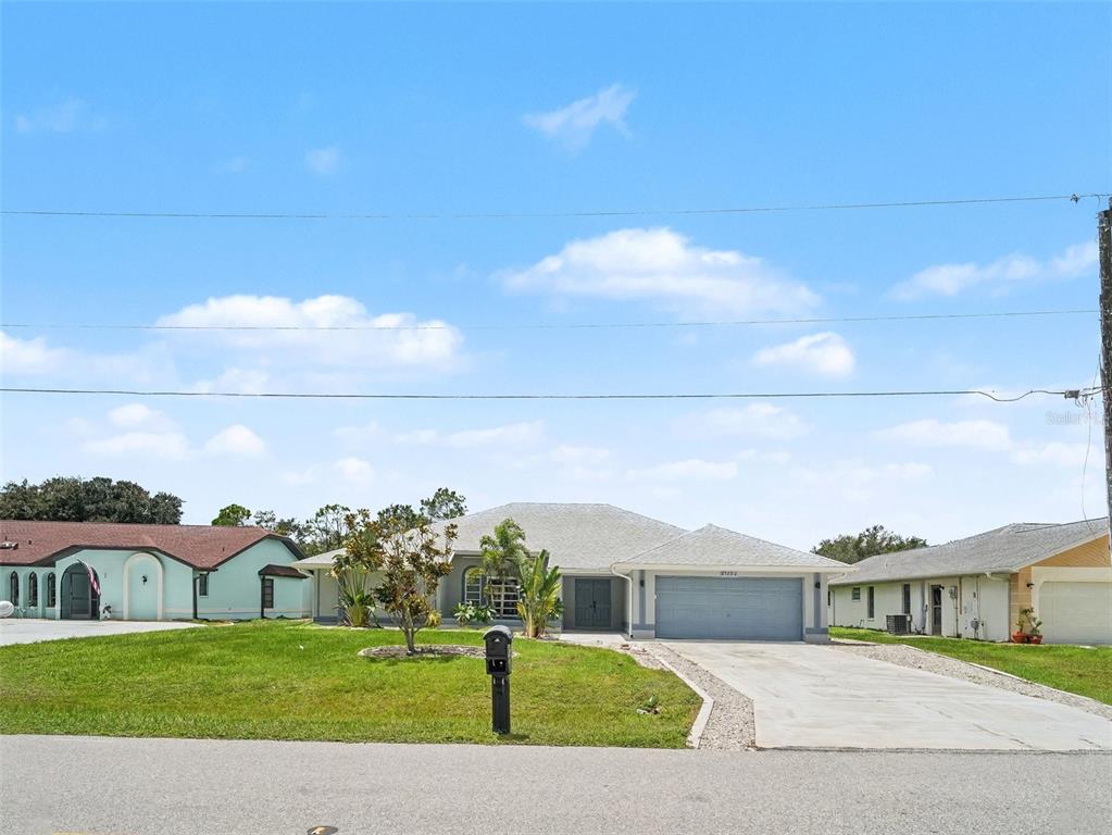 A single-story house with a gray garage and a front lawn under a blue sky — 25892 AYSEN DRIVE, PUNTA GORDA, FL