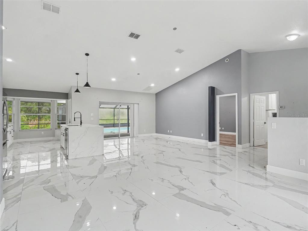 A spacious open-concept living area features white marble-look tile flooring, a kitchen island, and vaulted ceilings — 25892 AYSEN DRIVE, PUNTA GORDA, FL
