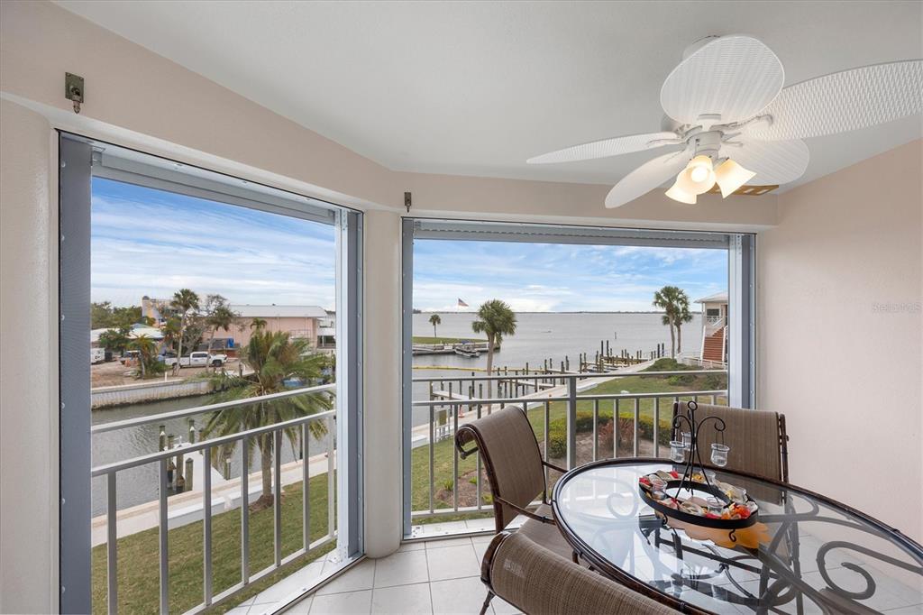A balcony with a dining set, ceiling fan, and views of a canal and bay — 11000 PLACIDA ROAD UNIT 2103, PLACIDA, FL