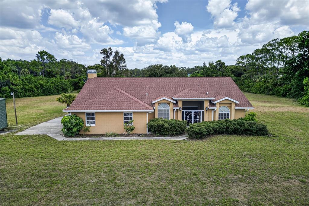 An exterior view of a tan, single-story house with a brown shingled roof and landscaping — 105 JACARANDA BOULEVARD, VENICE, FL