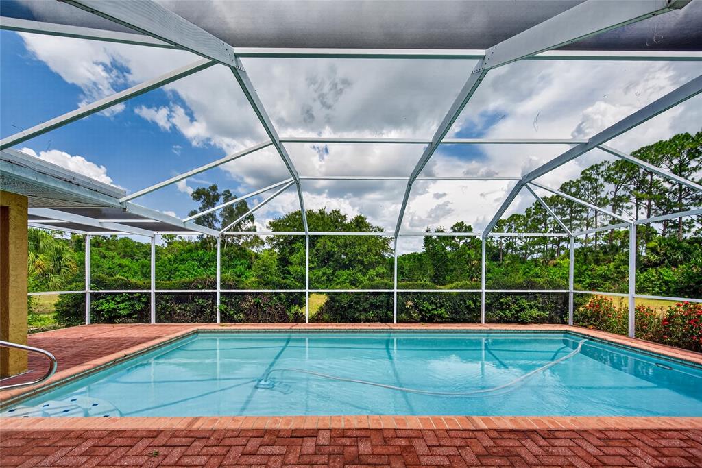 A rectangular swimming pool with a brick deck is enclosed by a white screen cage — 105 JACARANDA BOULEVARD, VENICE, FL