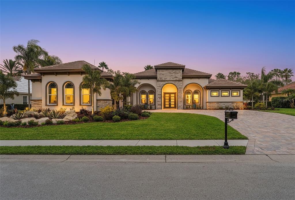 A single-story house with a stone facade, arched windows, and a paved driveway at dusk — 10700 PONTOFINO CIRCLE, TRINITY, FL