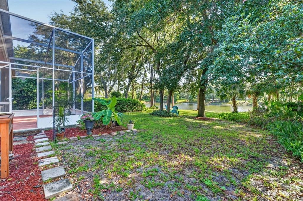 A screened-in patio overlooks a grassy backyard with trees and a small pond — 437 RANDON TERRACE, LAKE MARY, FL