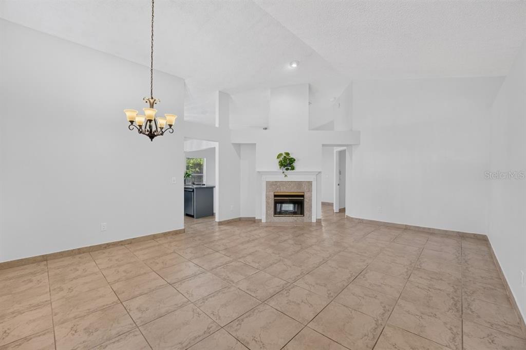 A living room with tile flooring, a fireplace, and a chandelier under a vaulted ceiling — 437 RANDON TERRACE, LAKE MARY, FL