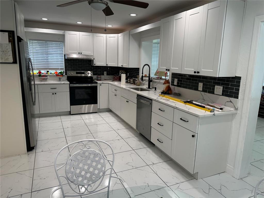 A kitchen with white cabinets, black subway tile backsplash, stainless steel appliances, and marble countertops — 17067 NW GAINESVILLE ROAD, REDDICK, FL