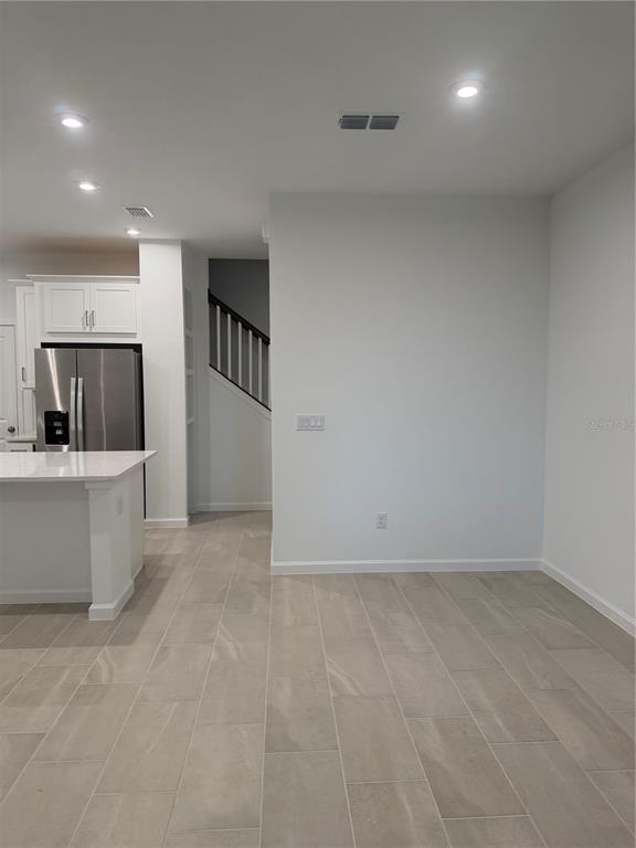 A kitchen with a white island and stainless steel refrigerator next to a staircase — 9972 RED CANOE ALLEY, ORLANDO, FL
