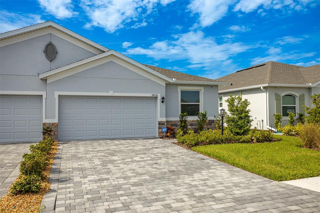 A gray house exterior features a paved driveway, stone accents, and a two-car garage — 18052 CROPSIDE TRAIL, BRADENTON, FL