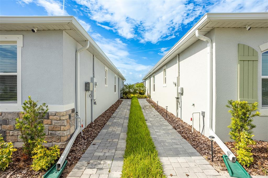 A narrow walkway with pavers and a central grass strip sits between two houses — 18052 CROPSIDE TRAIL, BRADENTON, FL