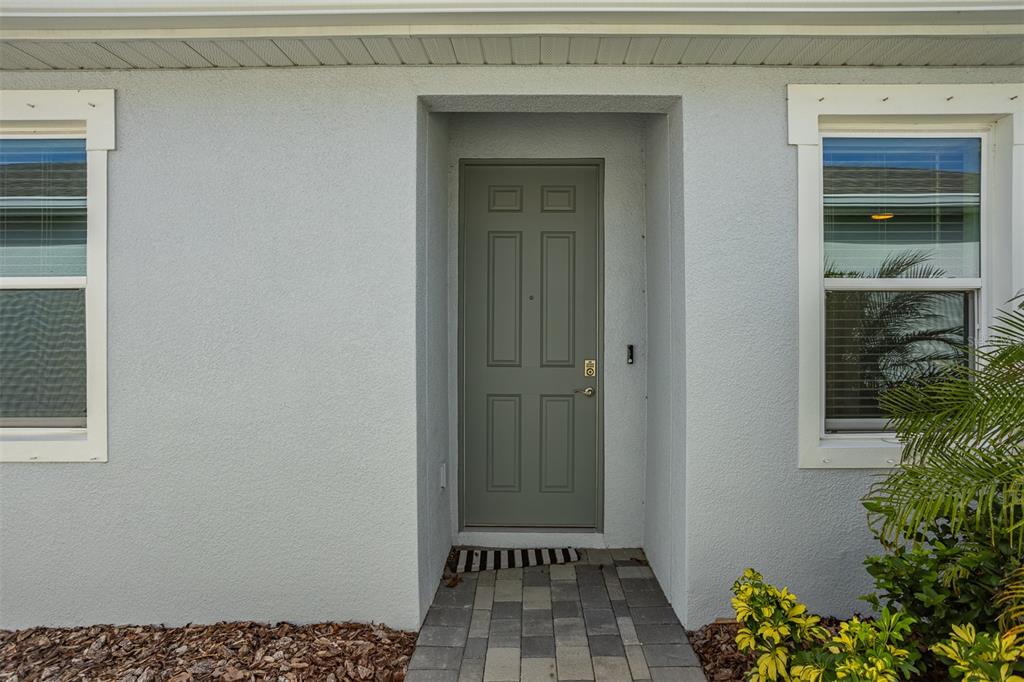 A gray front door is centered between two windows on a light-colored stucco exterior wall — 18052 CROPSIDE TRAIL, BRADENTON, FL