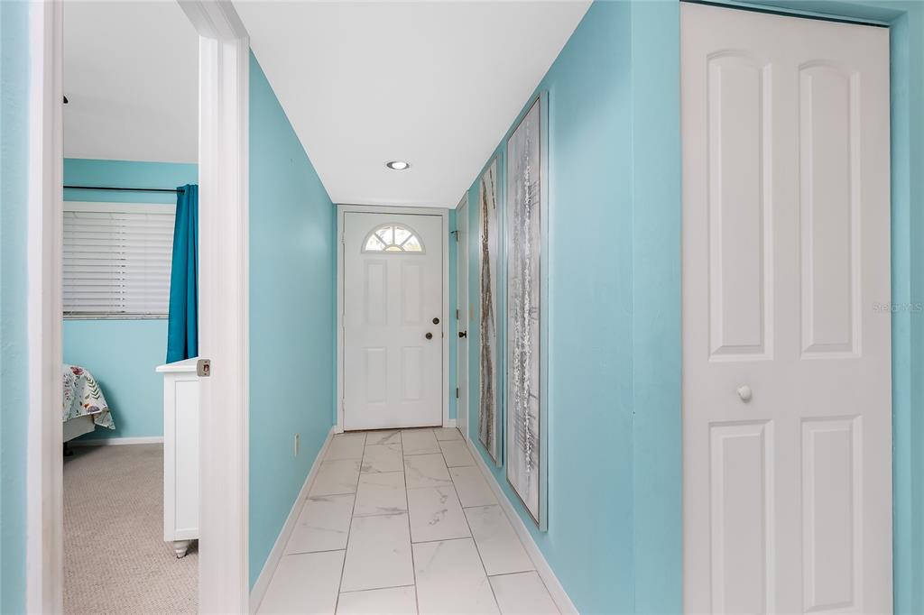 A bright hallway with light blue walls, white tile flooring, and a white front door — 6800 PLACIDA ROAD UNIT 1007, ENGLEWOOD, FL