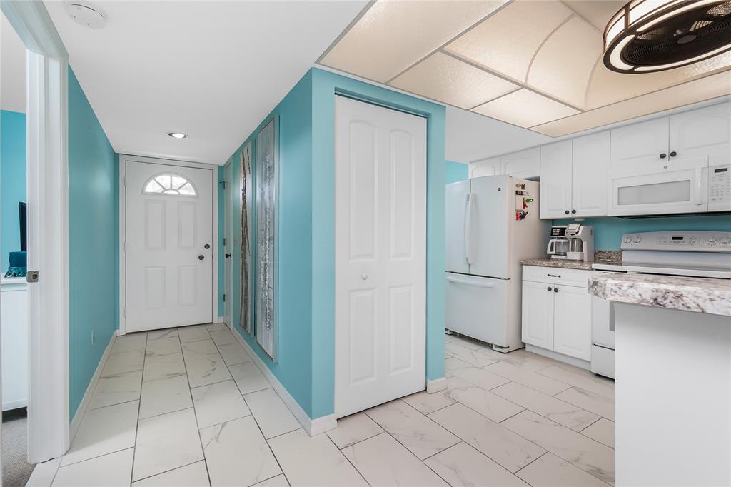 A kitchen and entryway feature white cabinets, light-colored tile flooring, and bright blue walls — 6800 PLACIDA ROAD UNIT 1007, ENGLEWOOD, FL