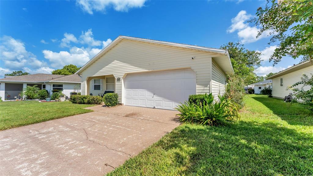 A light-colored house with a two-car garage and a concrete driveway under a blue sky — 2227 GRAND CYPRESS DRIVE, LAKELAND, FL