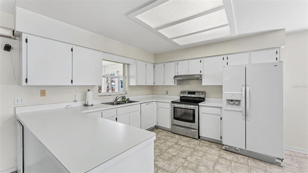 A kitchen features white cabinets, white countertops, stainless steel appliances, and tile flooring — 2227 GRAND CYPRESS DRIVE, LAKELAND, FL